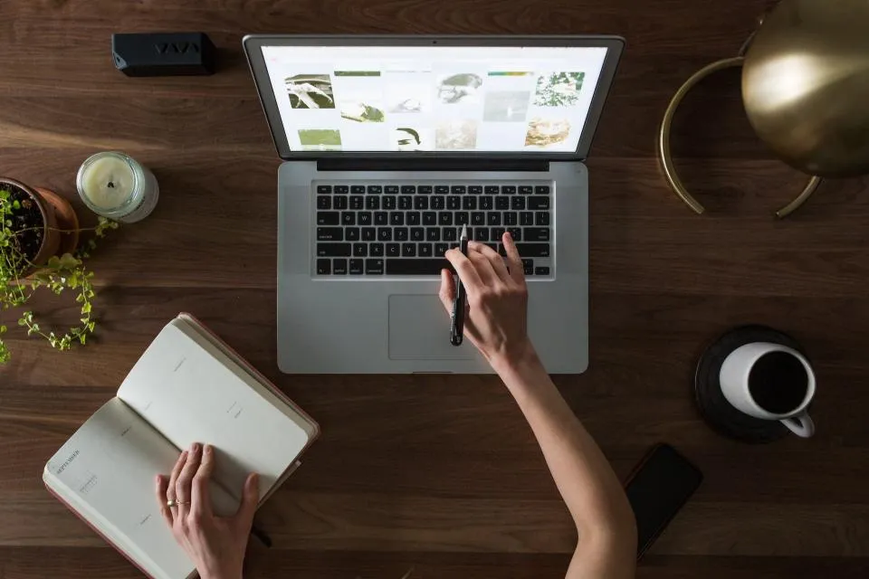 Looking down on a wooden desk with a laptop, an open notebook and a cup of coffee