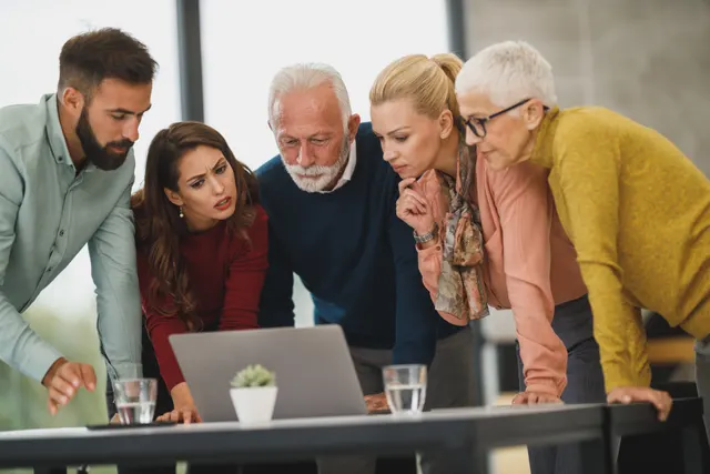 Five colleagues leaning in round a laptop to look at the screen together